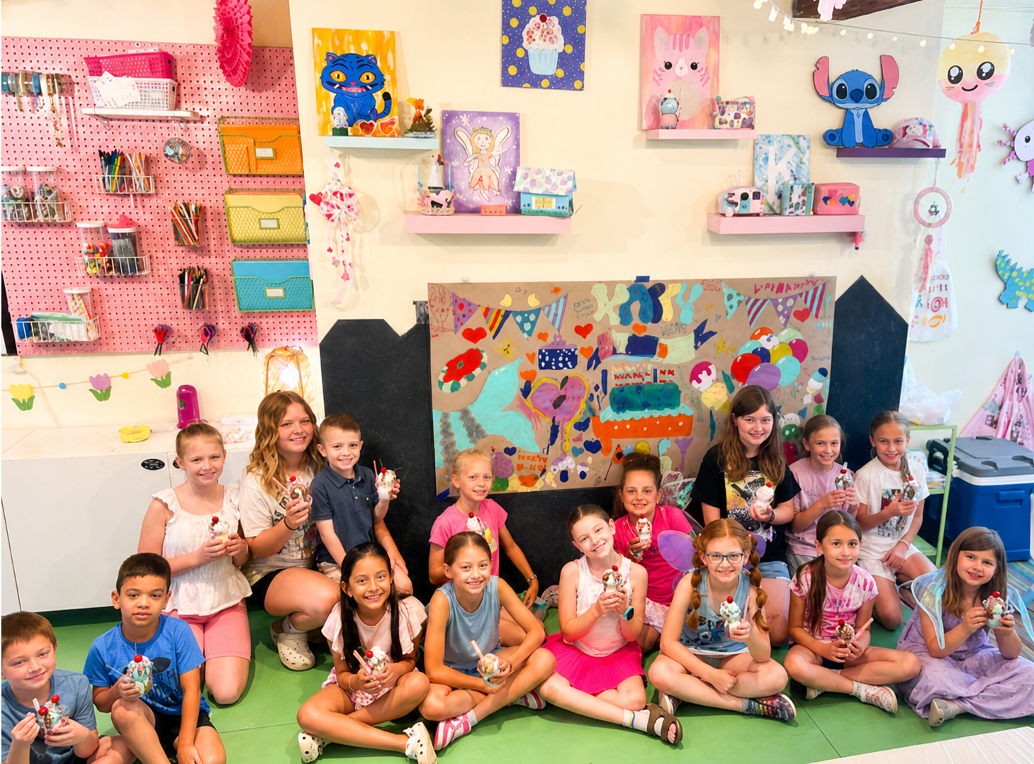 Kids birthday party displaying their artwork during art camp at Pink Art Pixie in Joppa, Maryland. Children and instructors smiling with their art projects during a kids’ art camp at Pink Art Pixie in Joppa, Maryland. A group of children and instructors showing their finished art projects inside Pink Art Pixie, a colorful children’s art studio in Joppa, MD offering art camps, classes and creative events.