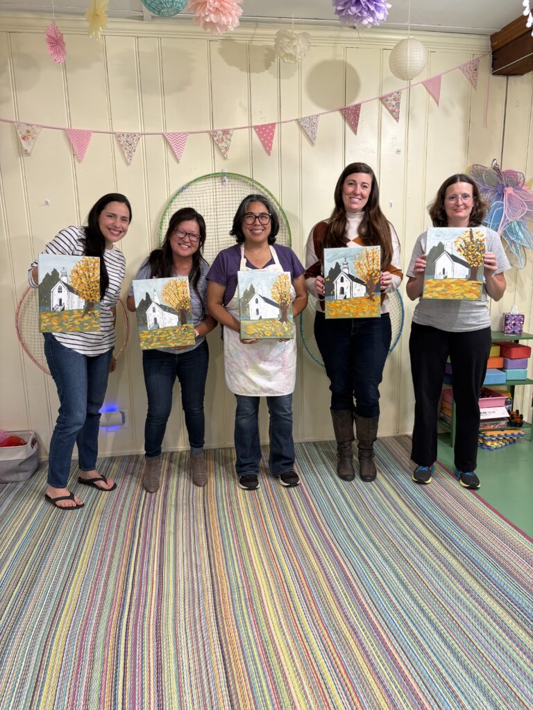 Adults displaying their finished canvas paintings during a Paint & Sip event at Pixieland in Joppa, Maryland. A group of adults proudly holds their completed paintings after a guided Paint & Sip workshop at Pixieland, home of Pink Art Pixie in Joppa, MD.
