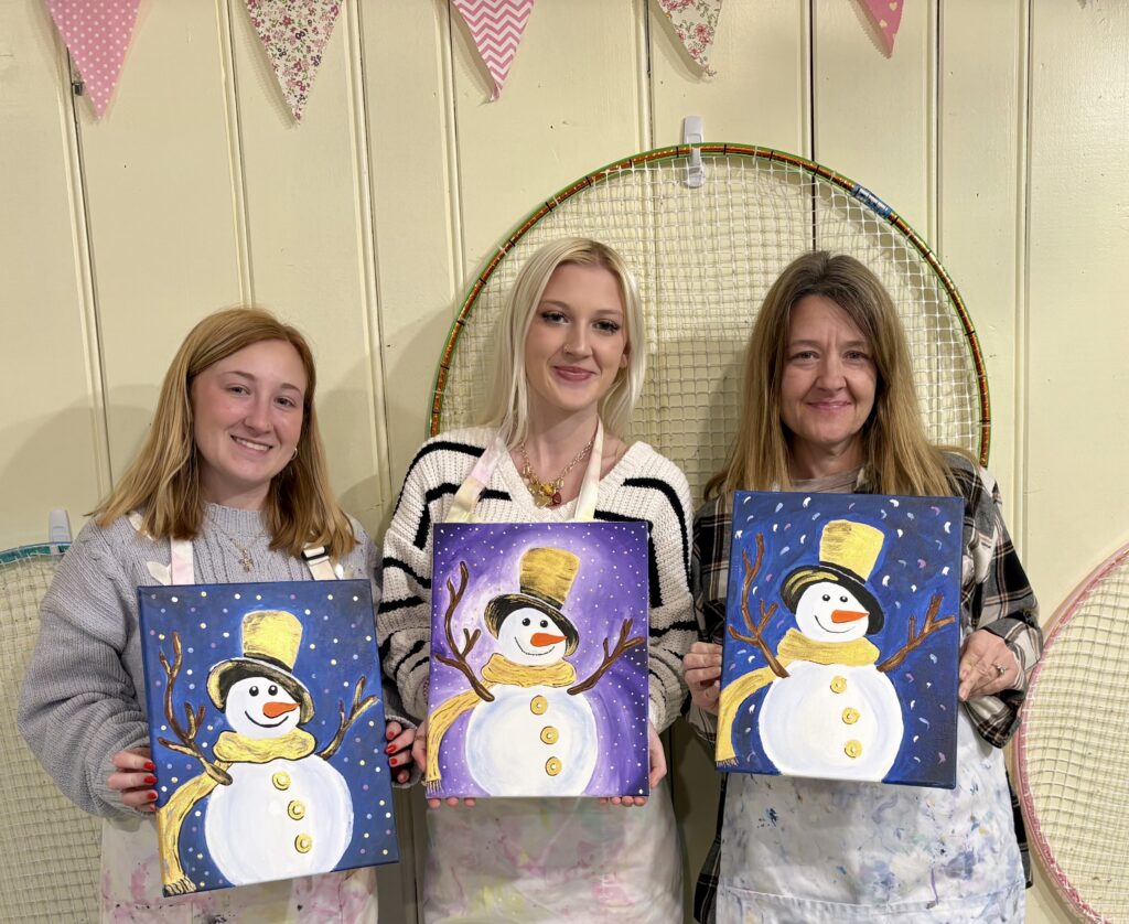 Three adults smiling and displaying their finished Jazzy Snowman canvas paintings during a Paint & Sip at Pink Art Pixie in Joppa, Maryland. Guests proudly hold their completed Jazzy Snowman paintings during a guided adult Paint & Sip workshop at Pink Art Pixie in Joppa, MD.Adults displaying Jazzy Snowman paintings at a Pink Art Pixie Paint & Sip.Adults displaying Jazzy Snowman paintings at a Pink Art Pixie Paint & Sip.
