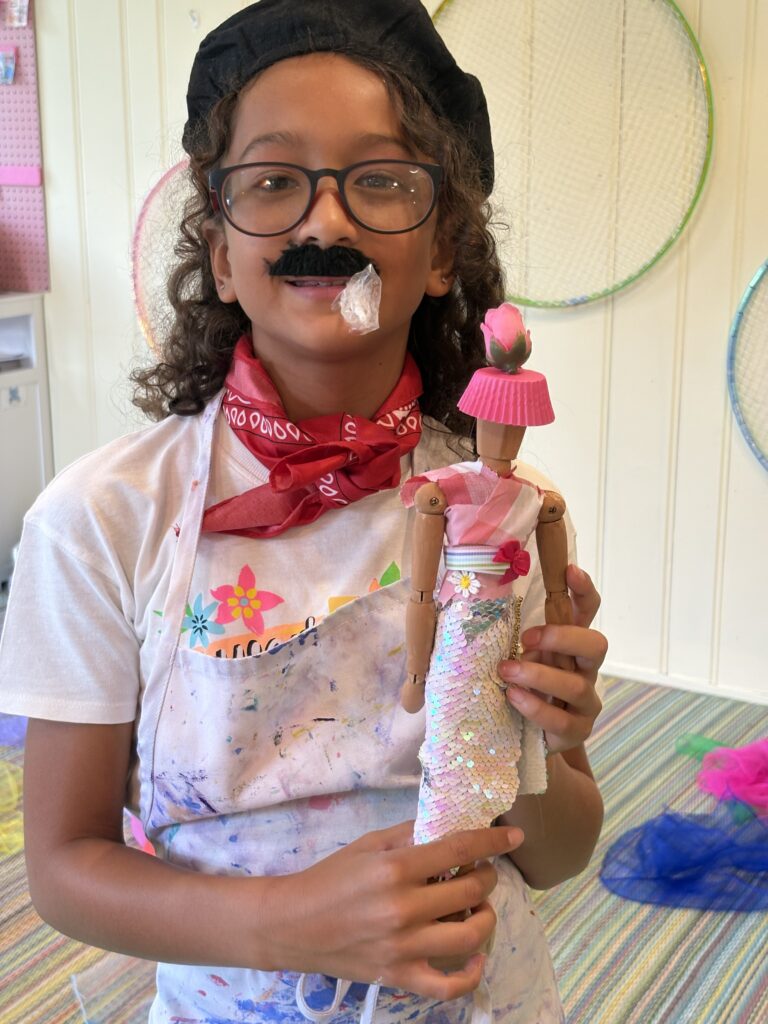Young artist dressed in a French-inspired costume holding an Eiffel Tower sculpture during Paris Art Camp at Pink Art Pixie in Joppa, Maryland
